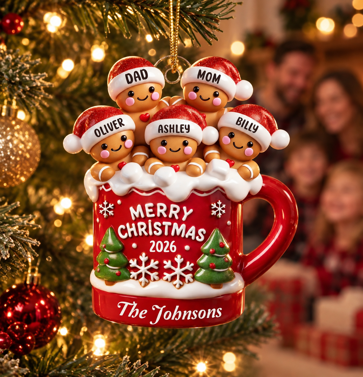 Personalized gingerbread family hot cocoa mug acrylic ornament on a Christmas tree with a family blurred behind
