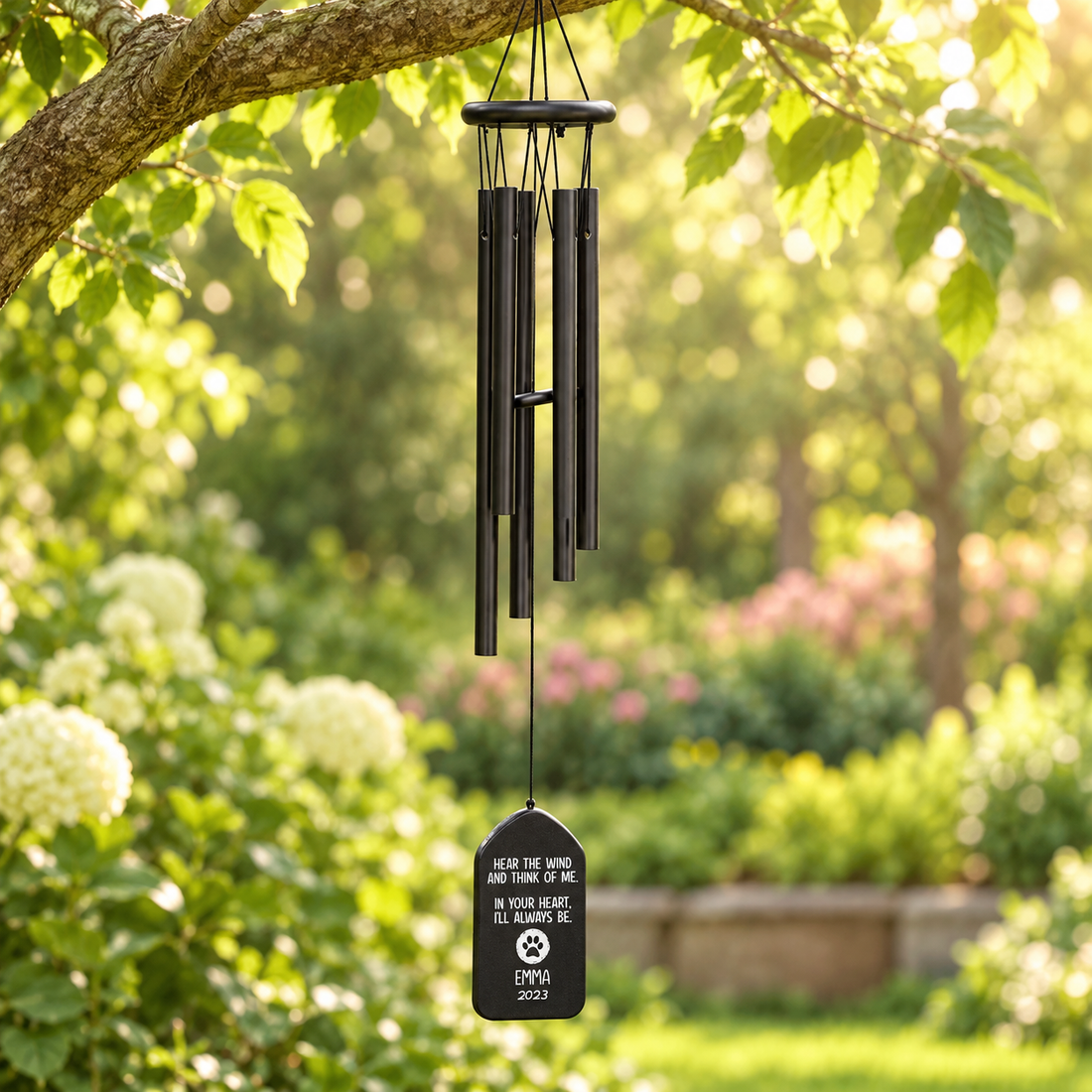 Personalized memorial wind chime with name plaque hanging from a tree in a sunny garden