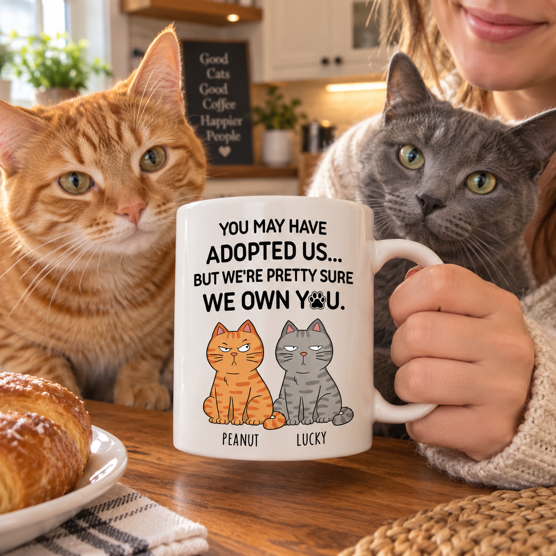 Funny cat mug with Peanut and Lucky cartoon cats held at a kitchen table beside real cats