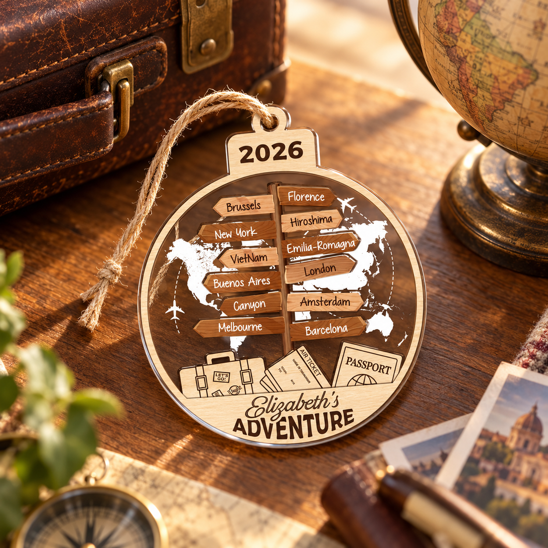 Personalized wooden travel destination ornament beside a vintage suitcase and a small globe