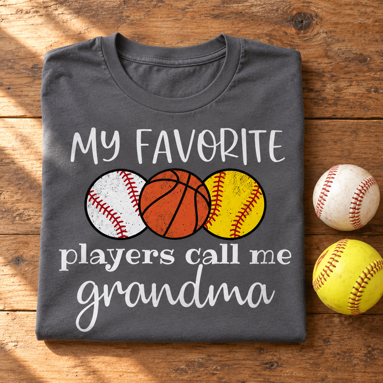 Personalized grandma sports t-shirt folded with a baseball and softball on a wooden table