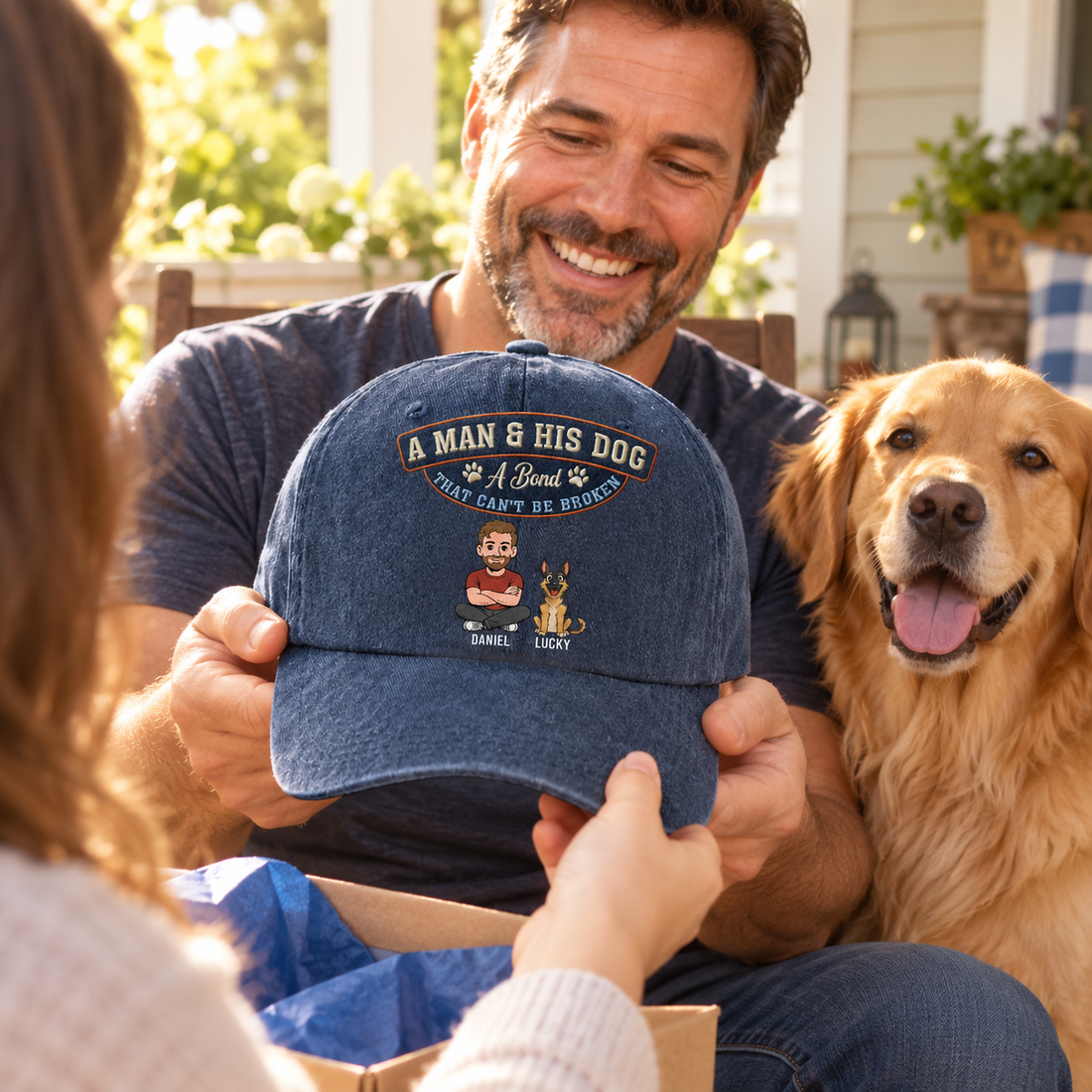 Man with golden retriever opening a personalized denim cap gift on a porch