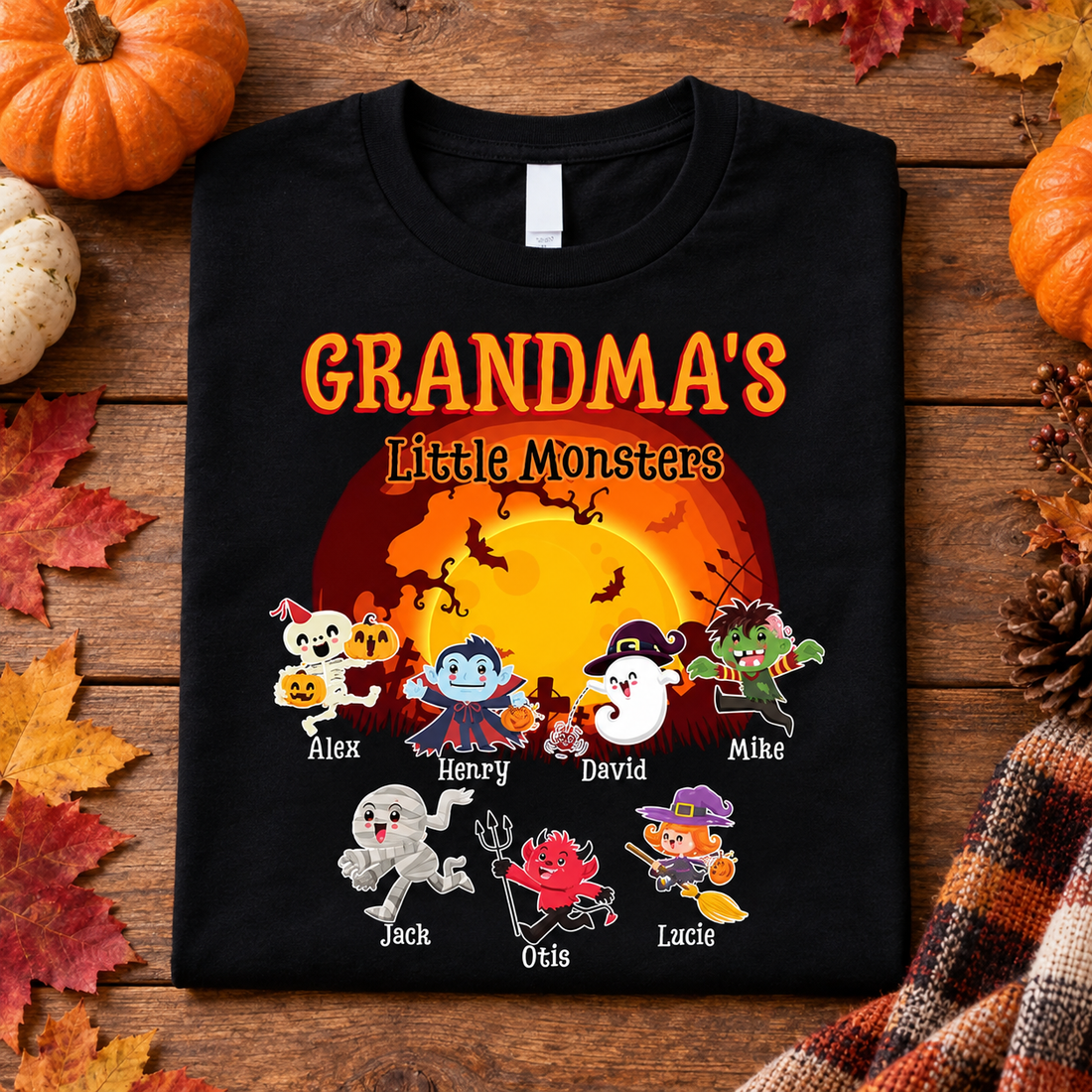 Black Grandma's Little Monsters personalized Halloween t-shirt flat lay with pumpkins and autumn leaves