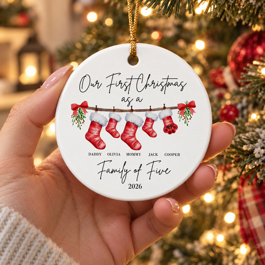 Mom's hand holding a personalized family ceramic Christmas ornament near the glowing tree