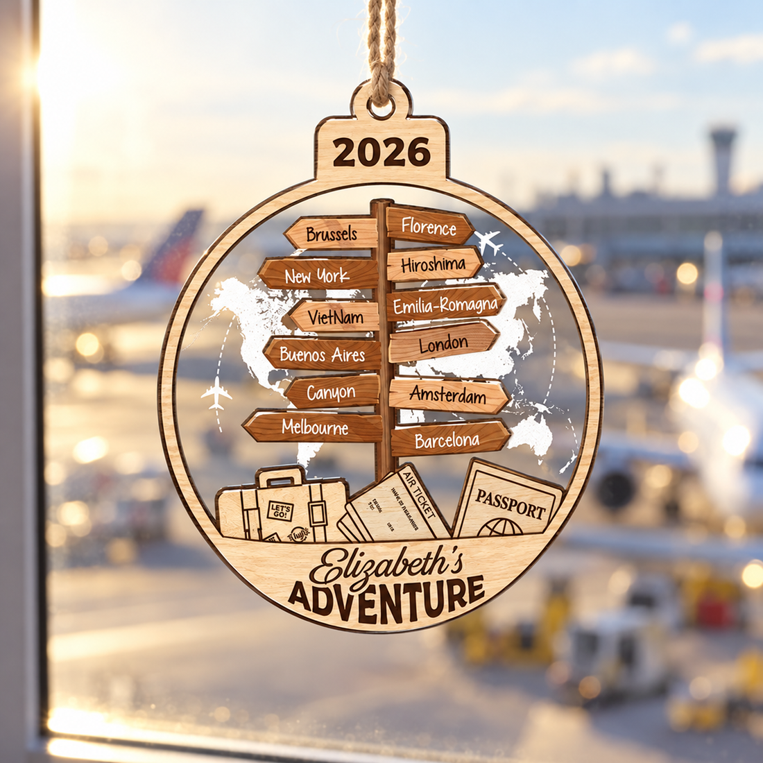 Custom travel destination ornament Elizabeth's Adventure hanging in a window with a sunny airport view