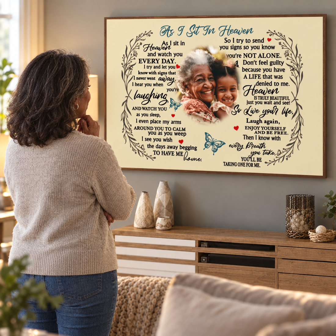 Woman looking at a personalized As I Sit In Heaven memorial poster on her living room wall
