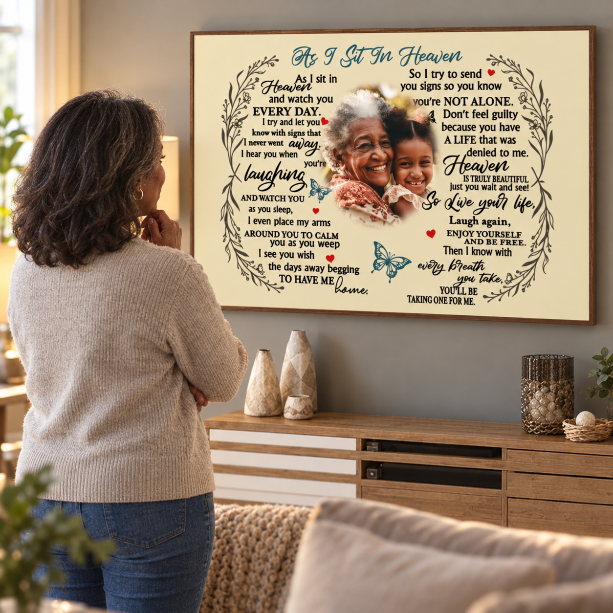 Woman looking at a personalized As I Sit In Heaven memorial poster on her living room wall