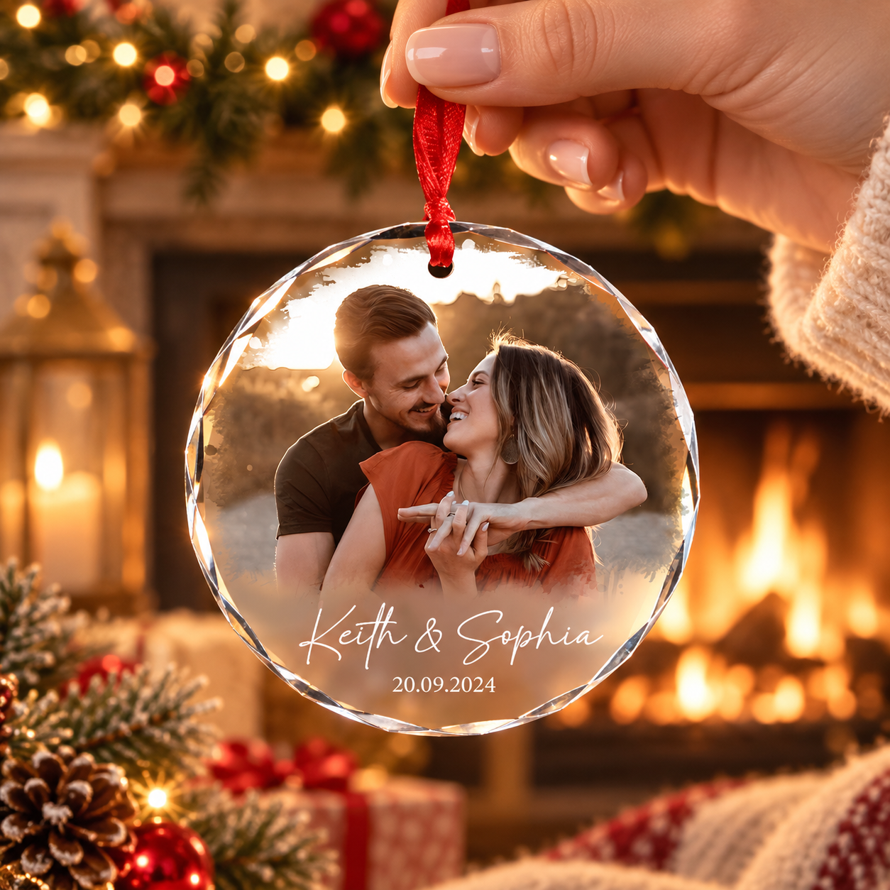 Hand holding a personalized crystal glass couple photo ornament in front of a lit fireplace