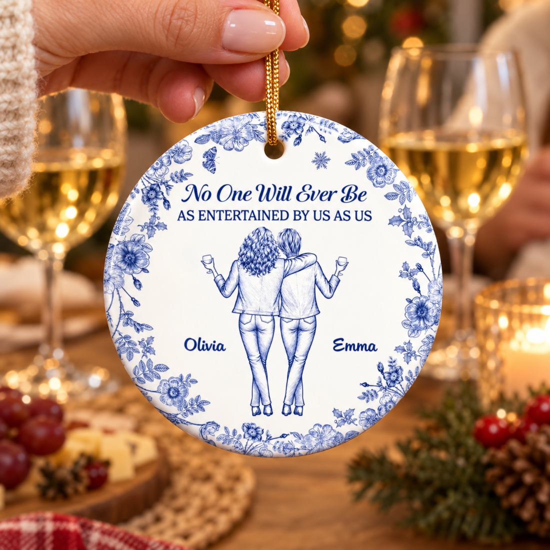 Hand holding a personalized bestie blue floral ceramic ornament beside two glasses of wine