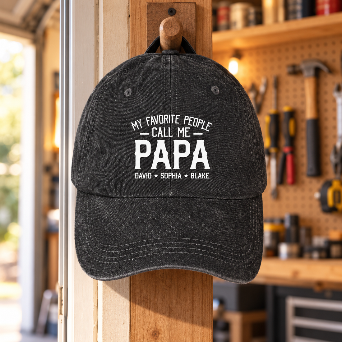 Black washed denim Papa cap with custom names hanging on a hook in a workshop