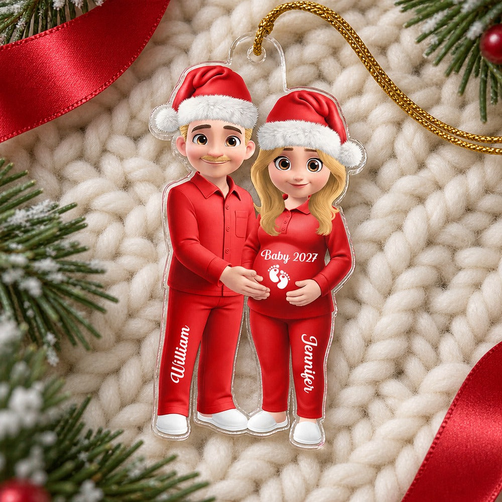 Expecting couple personalized acrylic Christmas ornament lying flat on a cream knit surface with greenery