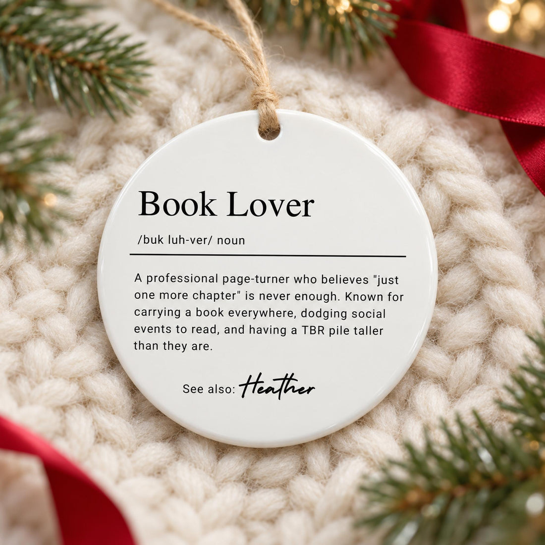 Personalized Book Lover ceramic ornament lying flat on a cream knit blanket with pine greenery
