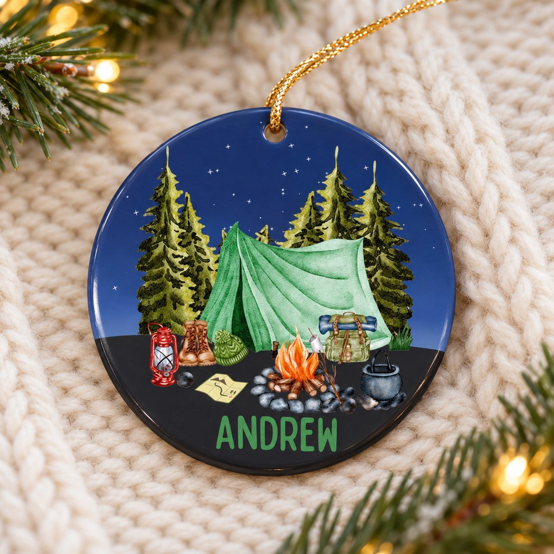 Camping tent personalized ceramic Christmas ornament lying flat on a cream knit throw with pine greenery