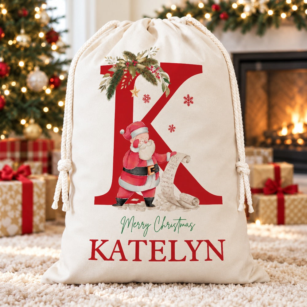 Personalized Katelyn Santa sack with red letter K standing by a Christmas fireplace and garland