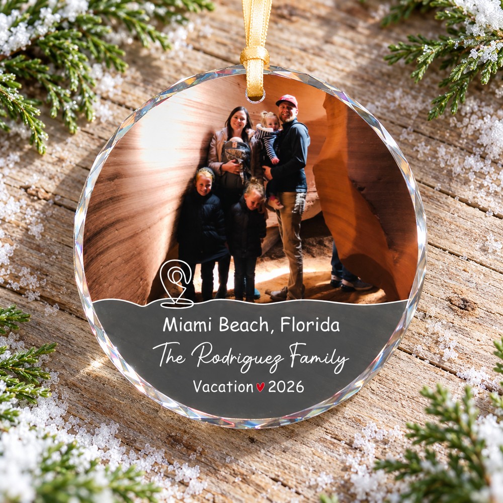 Custom family vacation keepsake glass ornament flat on rustic wood with winter greenery