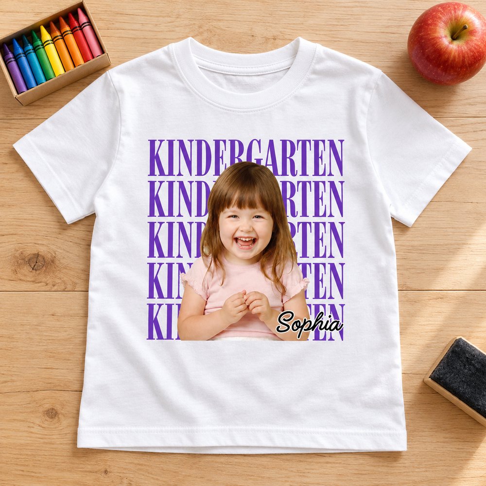White custom kindergarten photo kid shirt laid flat on wood table with crayons and apple
