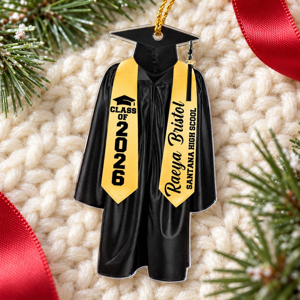 Custom graduation cap and gown ornament lying flat on cream knit fabric with holiday greenery