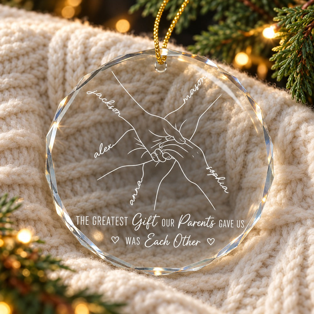 Custom sibling names glass ornament lying flat on a cozy cream knit throw with holiday greenery