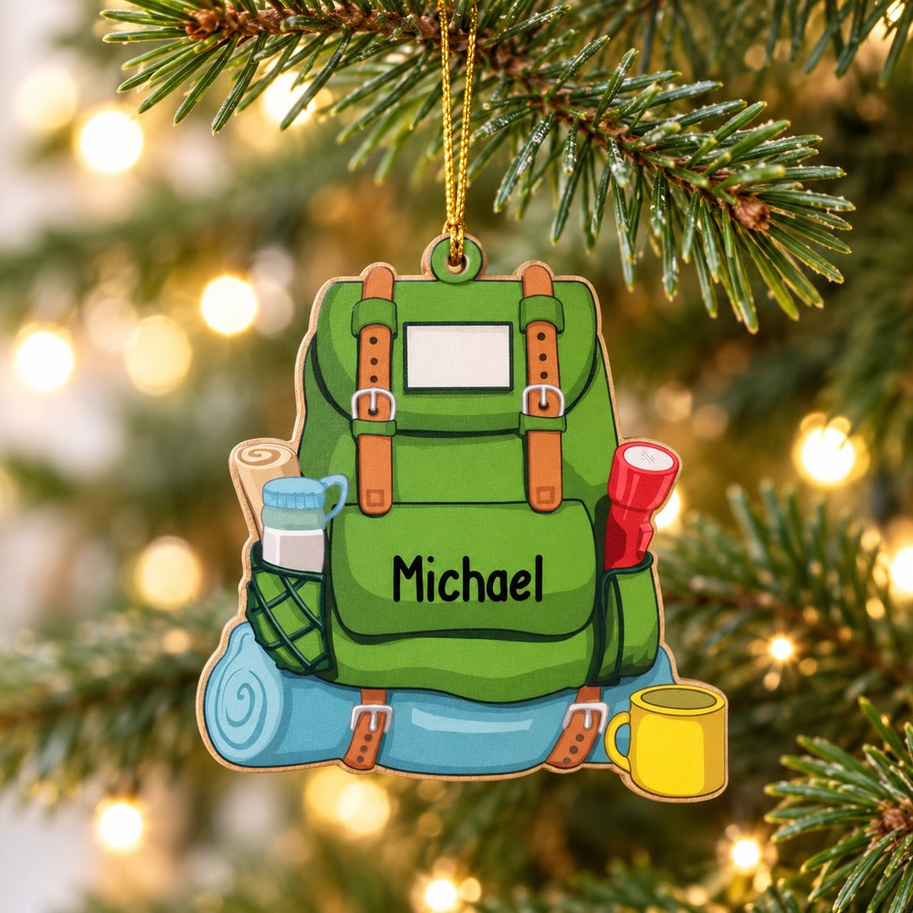 Personalized hiking backpack wood ornament hanging on a Christmas tree branch with warm lights