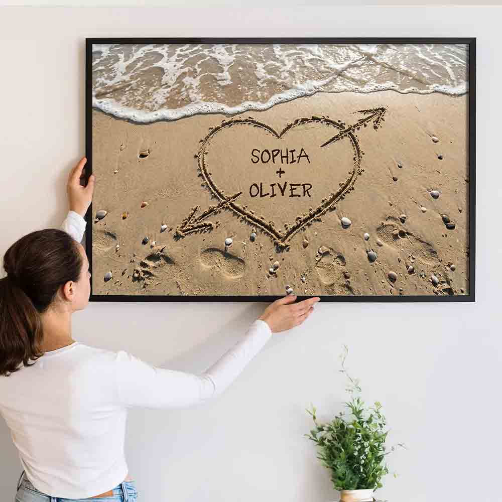 Personalized Couple Names Heart in Sand canvas print, a woman hanging the framed print on a wall