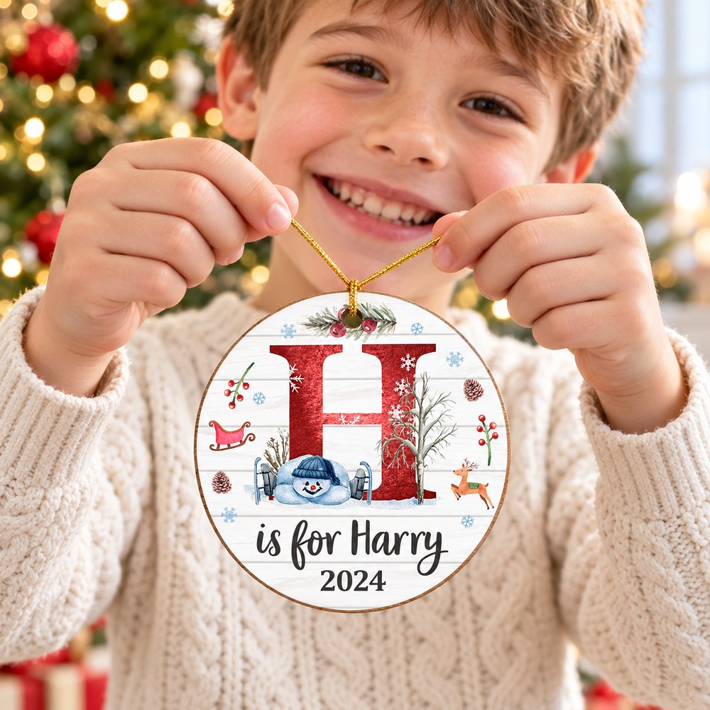 Child holding personalized H is for Harry 2024 circle wood Christmas ornament near tree