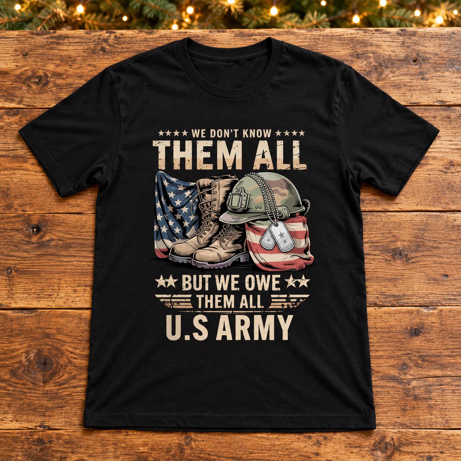 Patriotic We Owe Them All U.S Army black t-shirt laid flat with holiday greenery