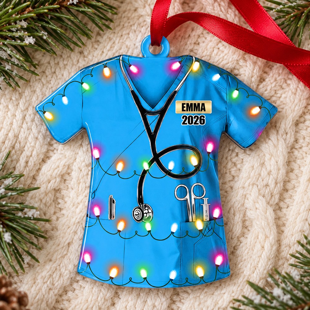 Custom nurse uniform acrylic ornament EMMA 2026 lying flat on cream knit fabric with holiday greenery