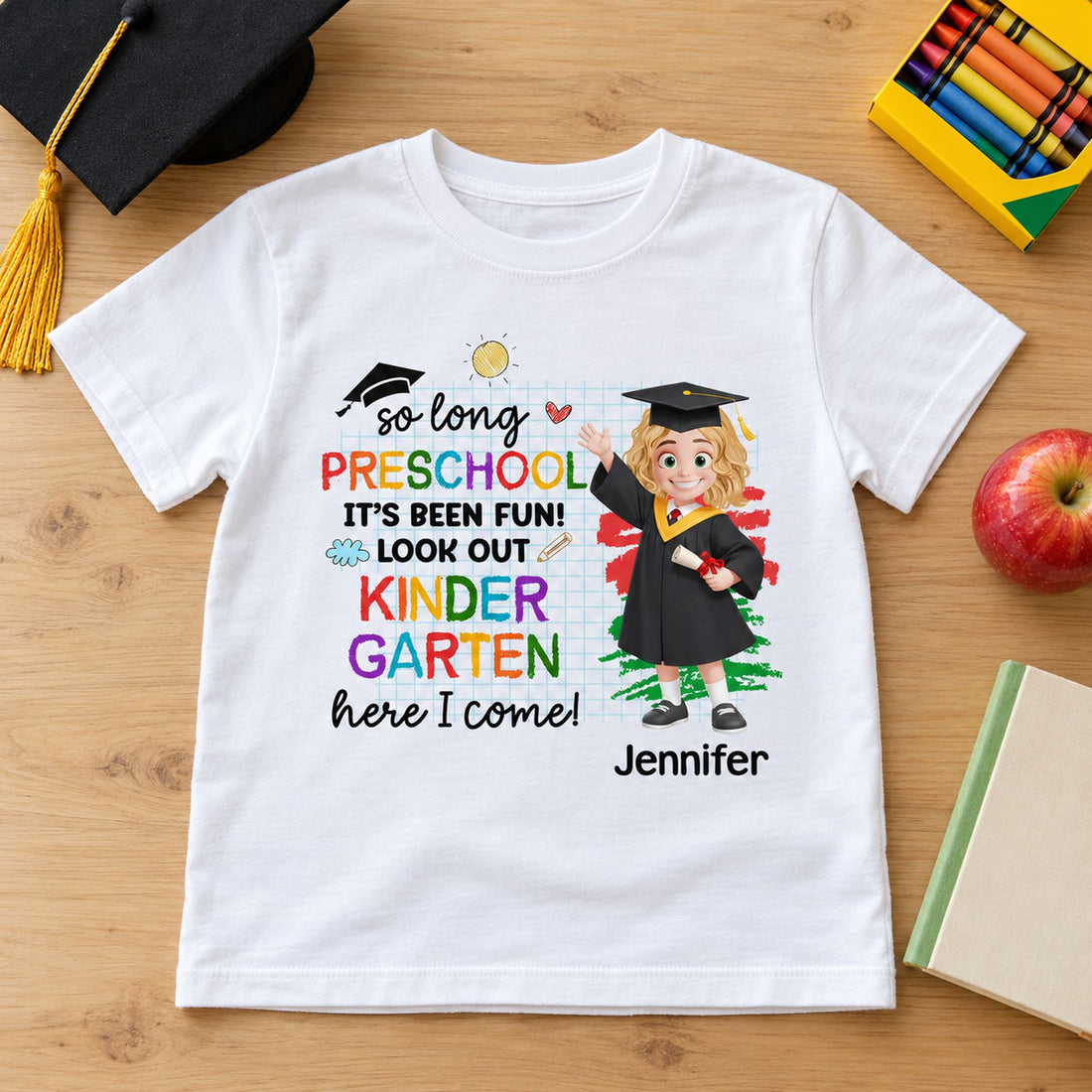 Personalized Kindergarten Here I Come kid t-shirt laid flat with crayons and graduation cap