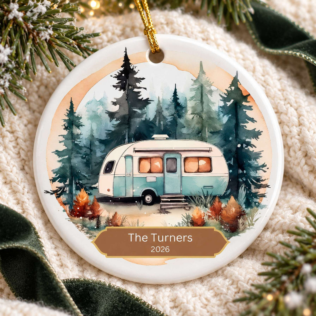 Custom camping trailer ceramic ornament lying flat on cream knit fabric with holiday greenery