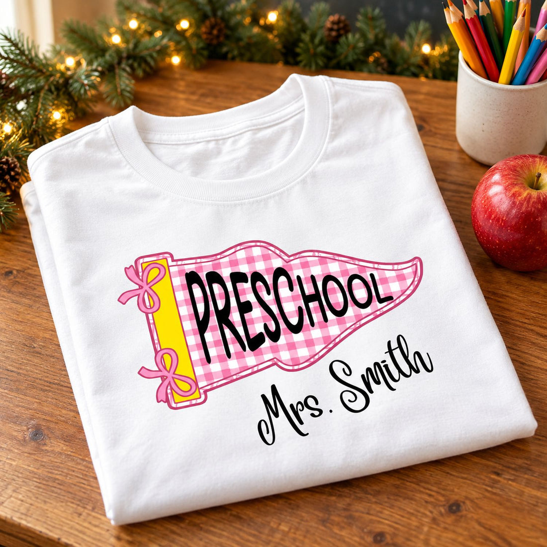 Folded personalized Preschool teacher pennant t-shirt on desk with apple and holiday garland