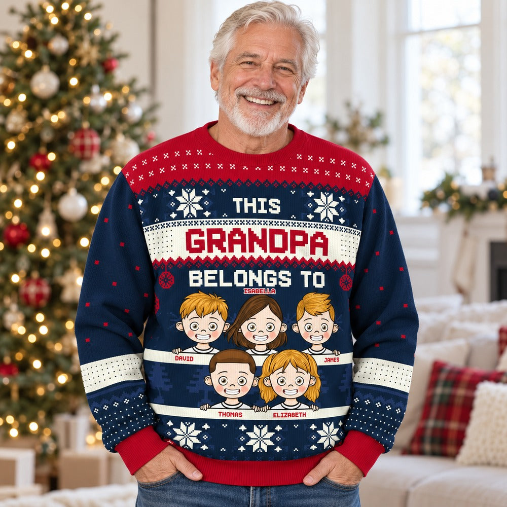 Grandpa wearing personalized This Grandpa Belongs To ugly Christmas sweater in front of a holiday tree
