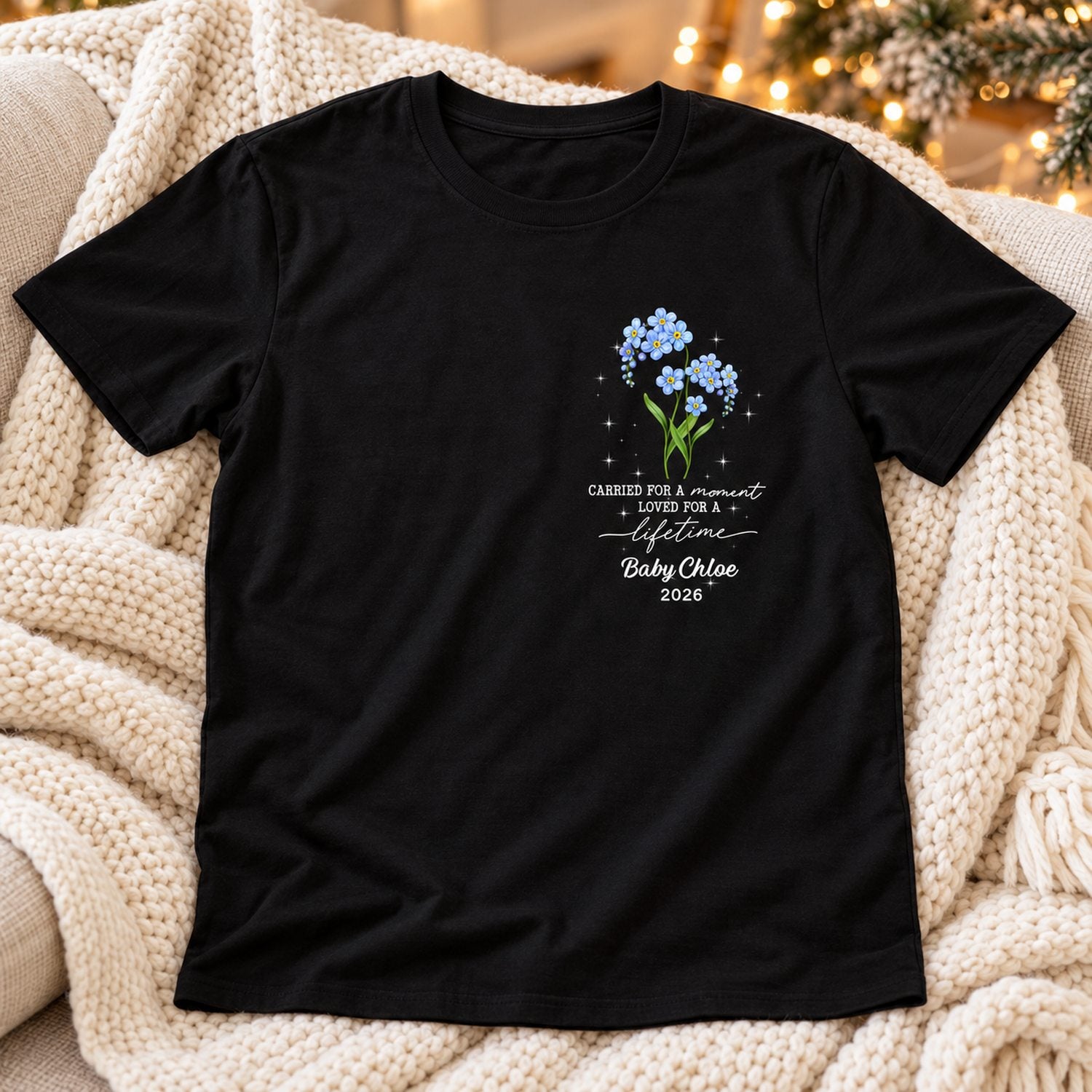 Personalized memorial t-shirt laid on a cozy sofa with soft holiday lights in the background