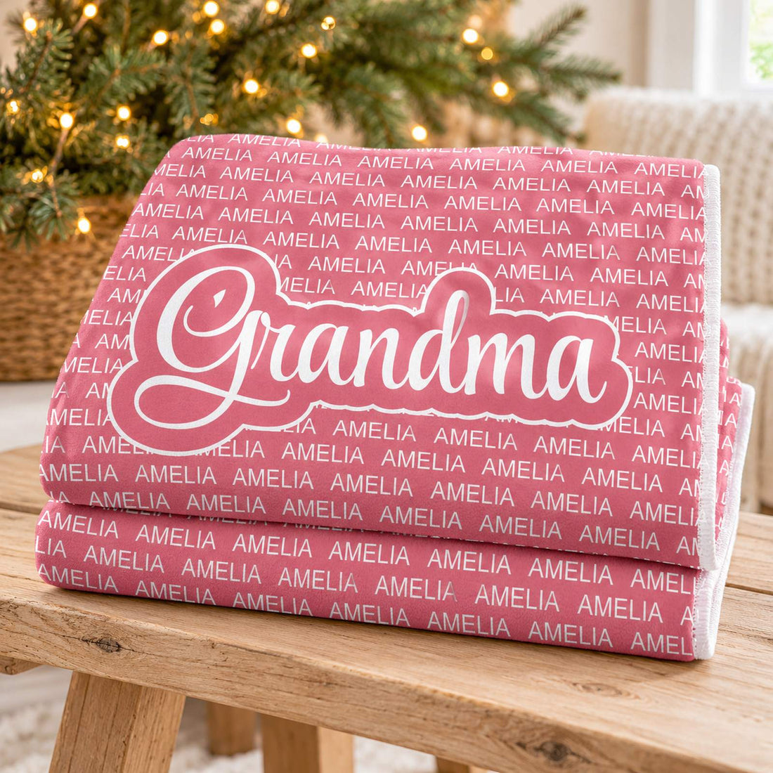 Folded personalized Grandma fleece blanket in dusty rose pink with holiday greenery in background
