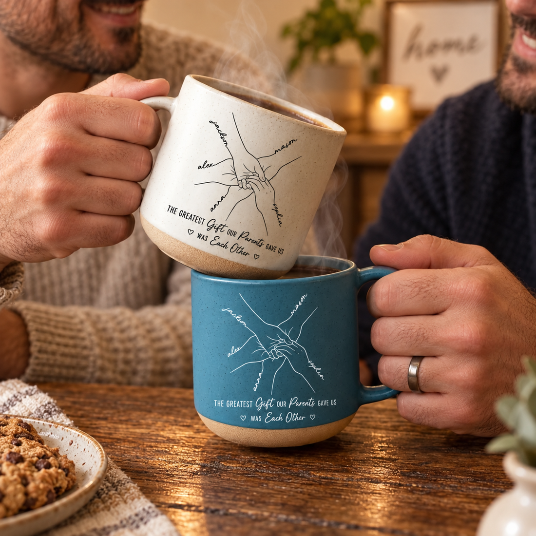 Two hands holding custom line-art handprint pottery mugs in white and blue on a wooden table