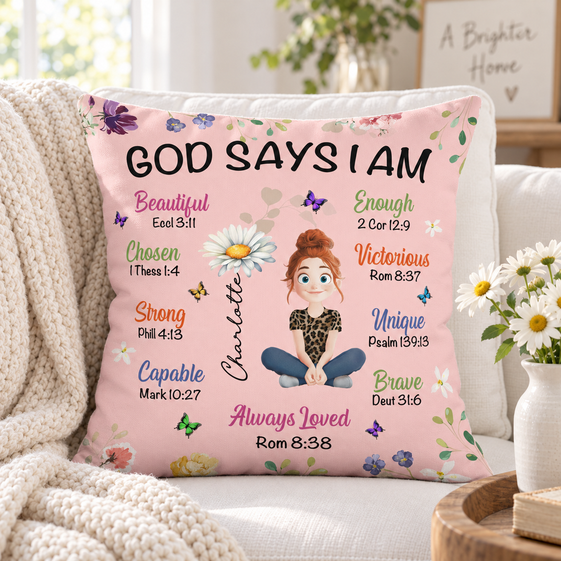 Pink God Says I Am birth flower pillow on a sofa with daisies and knit throw