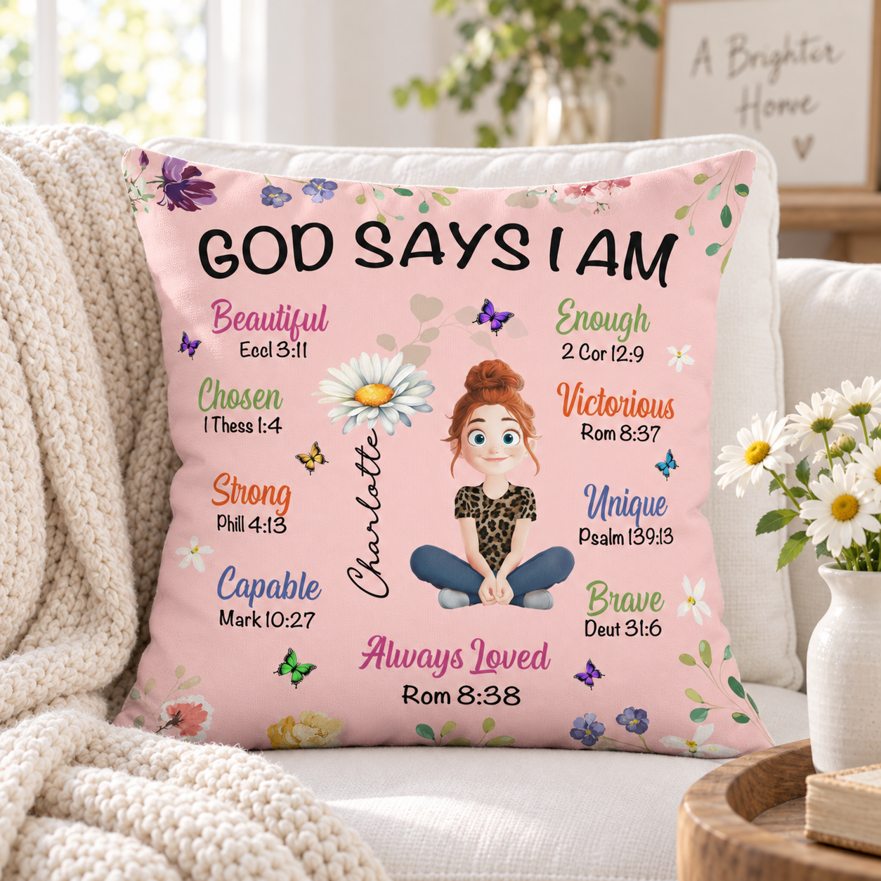 Pink God Says I Am birth flower pillow on a sofa with daisies and knit throw