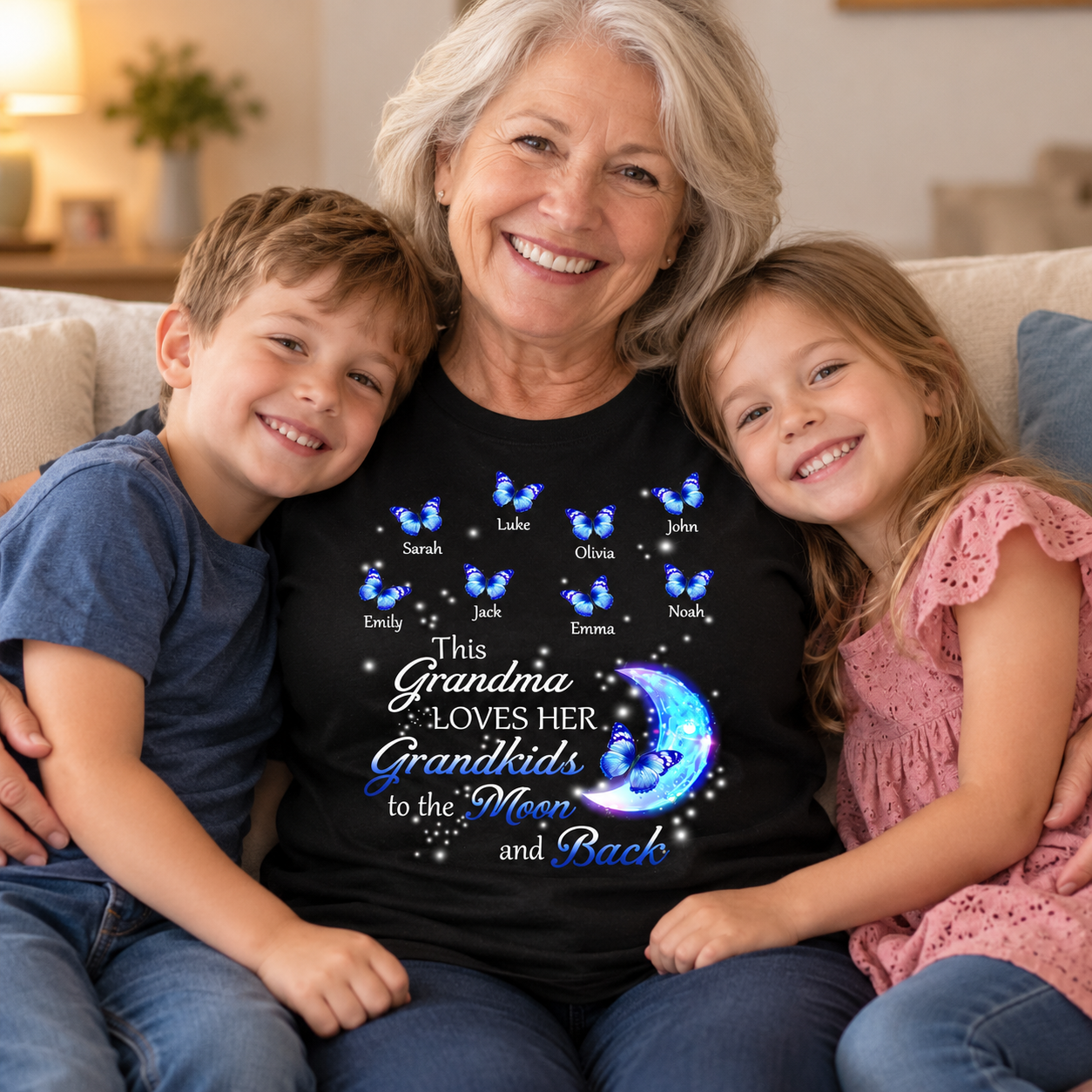 Smiling grandma in a black Grandma Loves Her Grandkids to the Moon and Back butterfly t-shirt hugging two grandkids