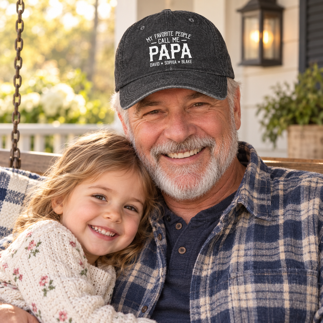 Grandpa wearing a My Favorite People Call Me Papa washed denim cap hugging his granddaughter on a porch swing