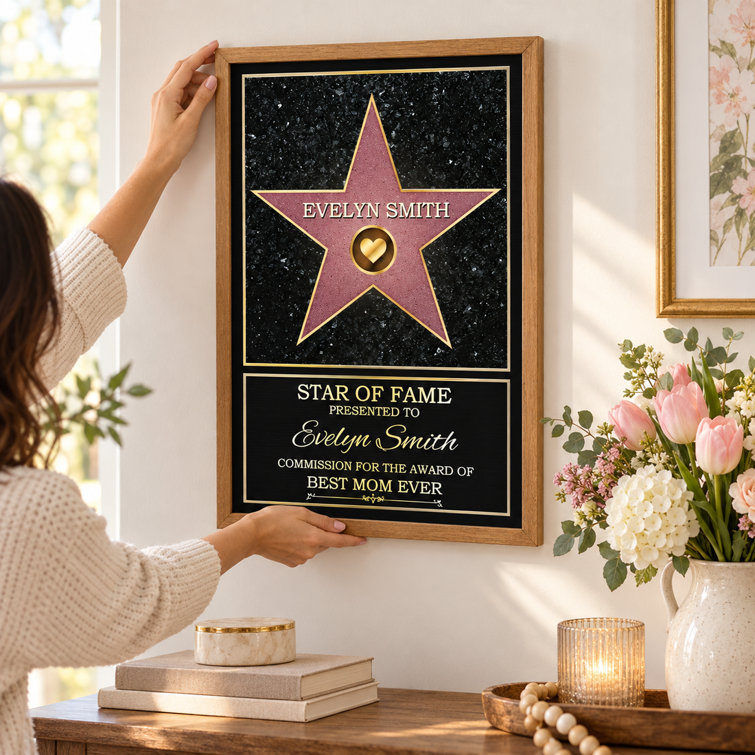 Hand adjusting a personalized Star of Fame Best Mom Ever framed poster on a wall above a console with flowers