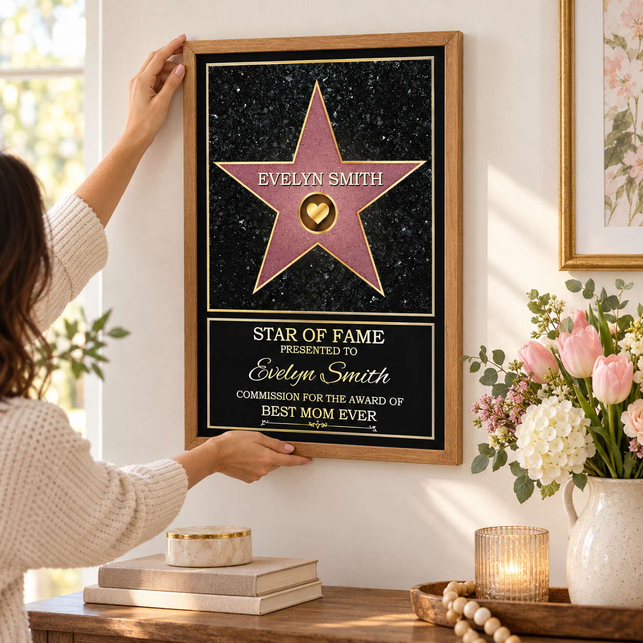 Hand adjusting a personalized Star of Fame Best Mom Ever framed poster on a wall above a console with flowers