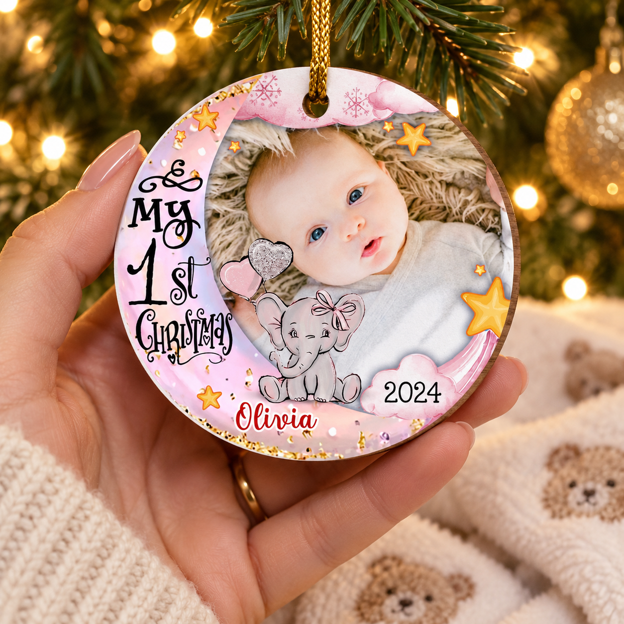 New mom's hand holding a personalized Baby's First Christmas wood ornament near the tree