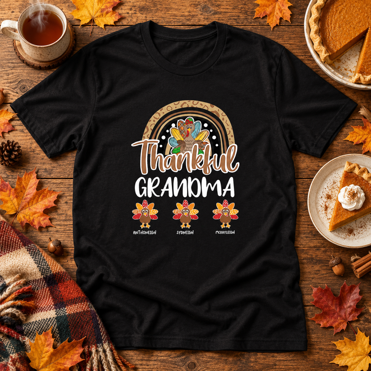 Flat lay of a personalized Thankful Grandma t-shirt on a wooden table with autumn leaves, tea and pie