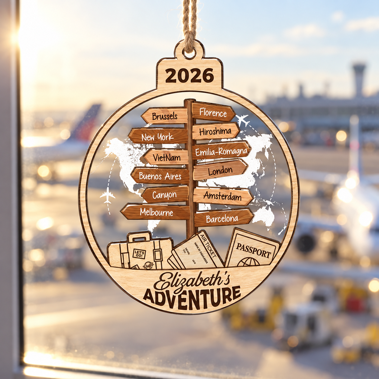 Custom travel destination ornament Elizabeth's Adventure hanging in a window with a sunny airport view