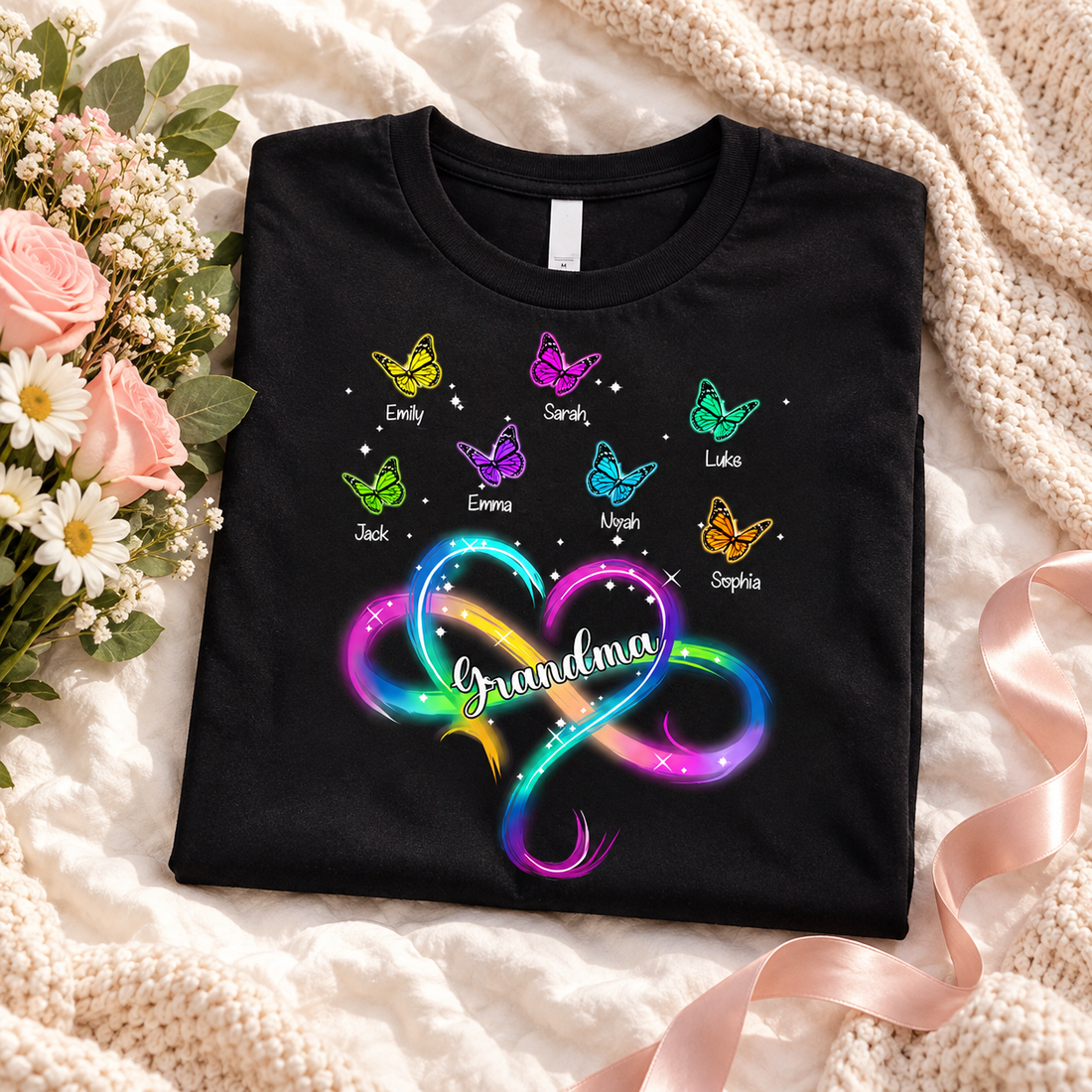 Black Grandma infinity heart butterfly t-shirt folded on a bed with flowers as a gift