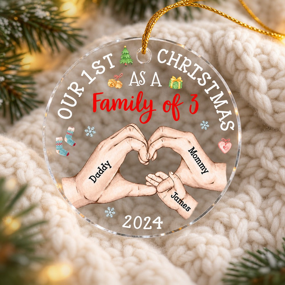 Baby First Christmas Family of 3 clear acrylic ornament lying on cream knit blanket with pine needles