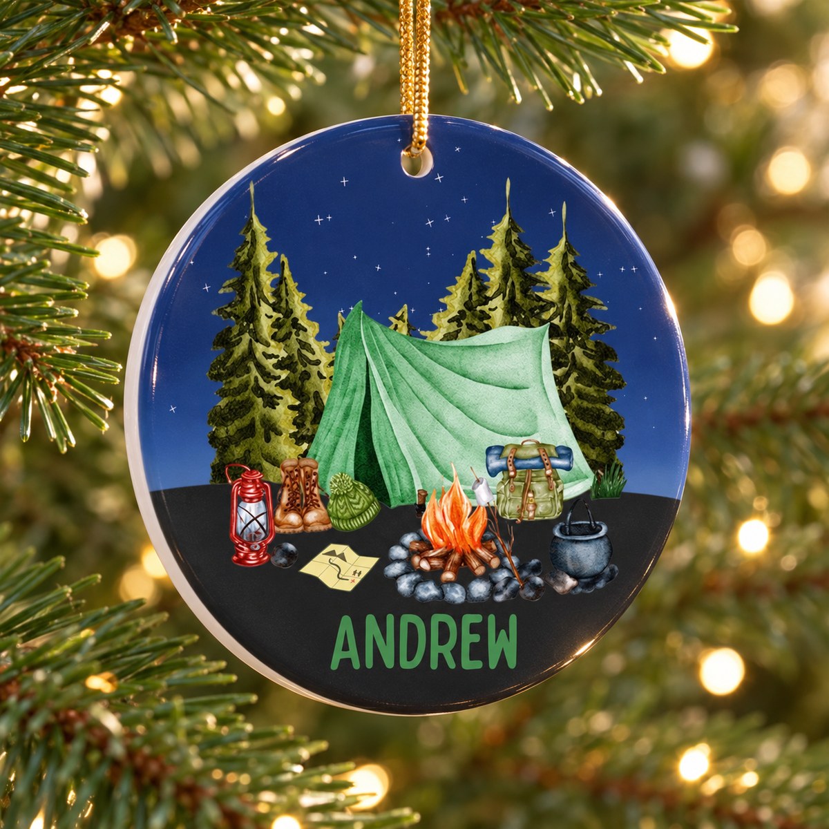 Close-up detail of glossy ceramic camping ornament showing campfire, tent print and ANDREW personalization