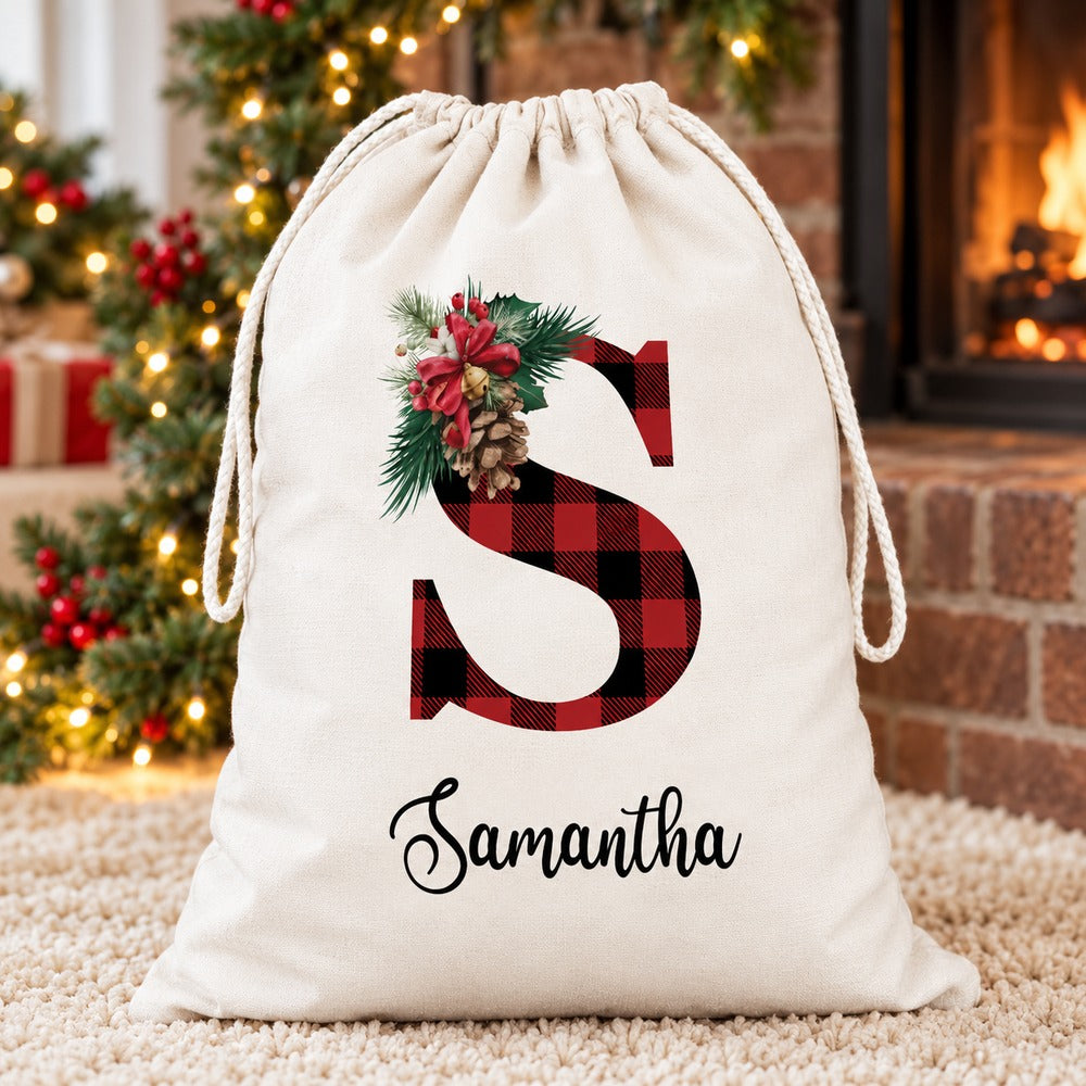 Personalized Samantha buffalo plaid Santa sack by a Christmas fireplace hearth