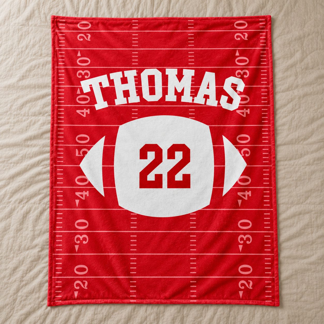 Custom Name and Number Football Team fleece blanket spread flat on a bed showing red gridiron design