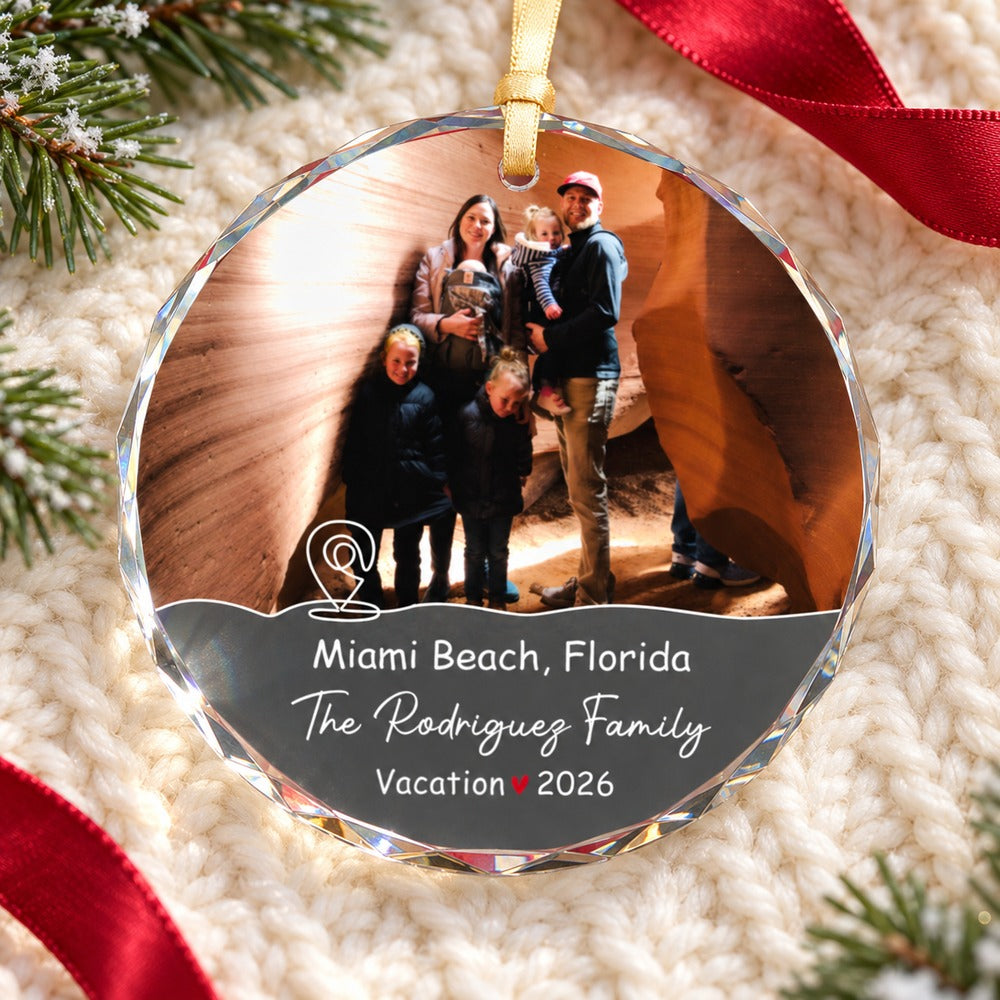 Personalized family vacation glass ornament lying flat on cozy cream knit fabric with pine