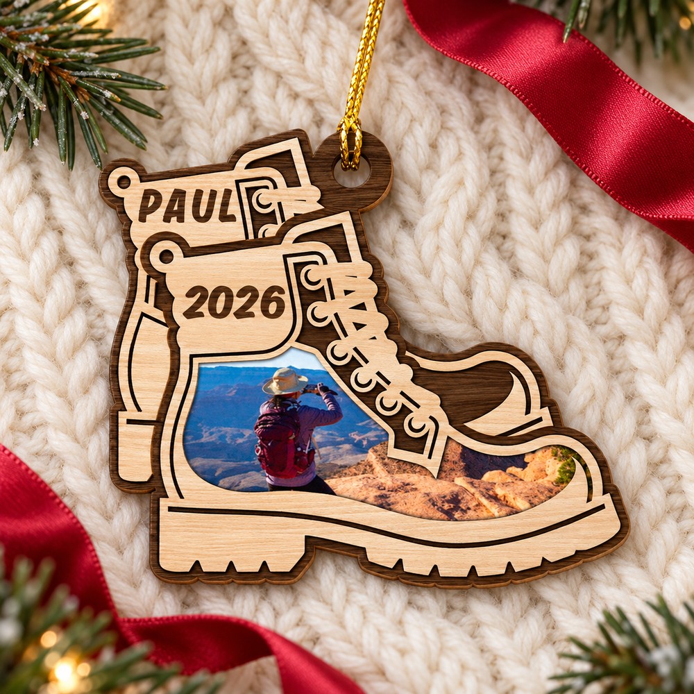 Personalized hiking boots Christmas wood ornament lying flat on a cream knit throw with pine greenery